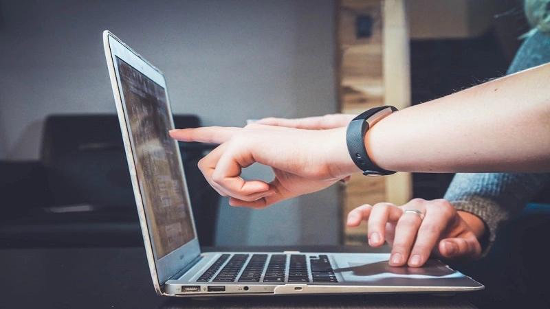 Collaborative professionals using cloud-based knowledge management software, pointing out features and ensuring efficient workflow on a laptop.